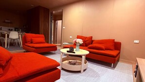 Un salon moderne avec des canapés rouges, une table basse ronde et un coin repas à l’arrière-plan.