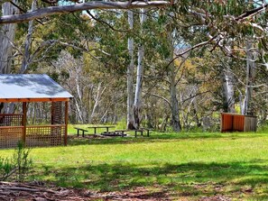 A picnic area with a wooden shelter, picnic tables, and a small shed in a wooded park.