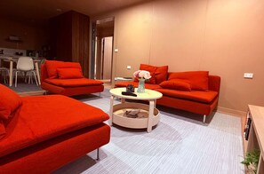 A modern living room with red sofas, a round coffee table, and a dining area in the background. - Your gateway to an unforgettable holiday experience in the stunning Snowy Mountains! (Adaminaby)