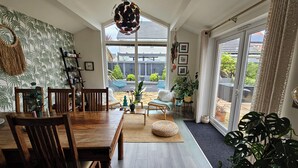 Un espace repas avec une table et des chaises en bois, un luminaire suspendu et une vue sur la terrasse extérieure à travers de grandes fenêtres.