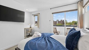 A hotel room with a bed, a desk, a chair, a TV, and a balcony with a view of buildings. - Perch - Capitol Luxe B | Prime Location in Cap Hill | Walk Score 93 (Seattle)
