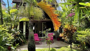 A tropical garden with palm trees, a thatched roof structure, and a patio area with chairs. - Paradise House in Trou-aux-biches (Mont Choisy)