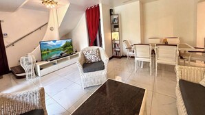 A modern living room with a flat-screen TV, wicker furniture, a bookshelf, and a staircase. - Paradise House in Trou-aux-biches (Mont Choisy)