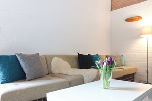Een woonkamer met een beige bank, een witte tafel en een vaas met bloemen.