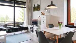 Una sala de estar moderna con comedor, ventanas grandes y vista a árboles.