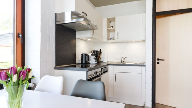 Una cocina moderna con armarios blancos, una campana extractora de acero inoxidable y una cafetera.