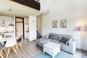 A modern living room with a grey sofa, a white coffee table, and a dining area with a white table and chairs. - Apartment with 2 bedrooms (Braunlage)