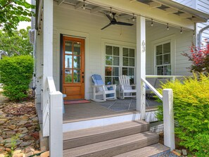 Eine Veranda mit einer Holztür, zwei Adirondack-Stühlen und einem kleinen Tisch.