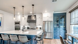 Una cocina moderna con una isla grande, taburetes de bar, electrodomésticos de acero inoxidable y un armario azul.
