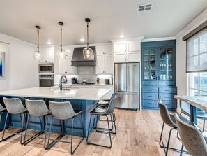 Eine moderne Küche mit einer großen Kochinsel, Barhocker, Edelstahlgeräten und einem blauen Schrank.