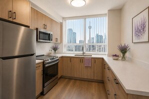 Eine moderne Küche mit Edelstahlgeräten, Holzschränken, einem großen Fenster mit Blick auf die Stadt und einer Vase mit Blumen auf der Arbeitsplatte.