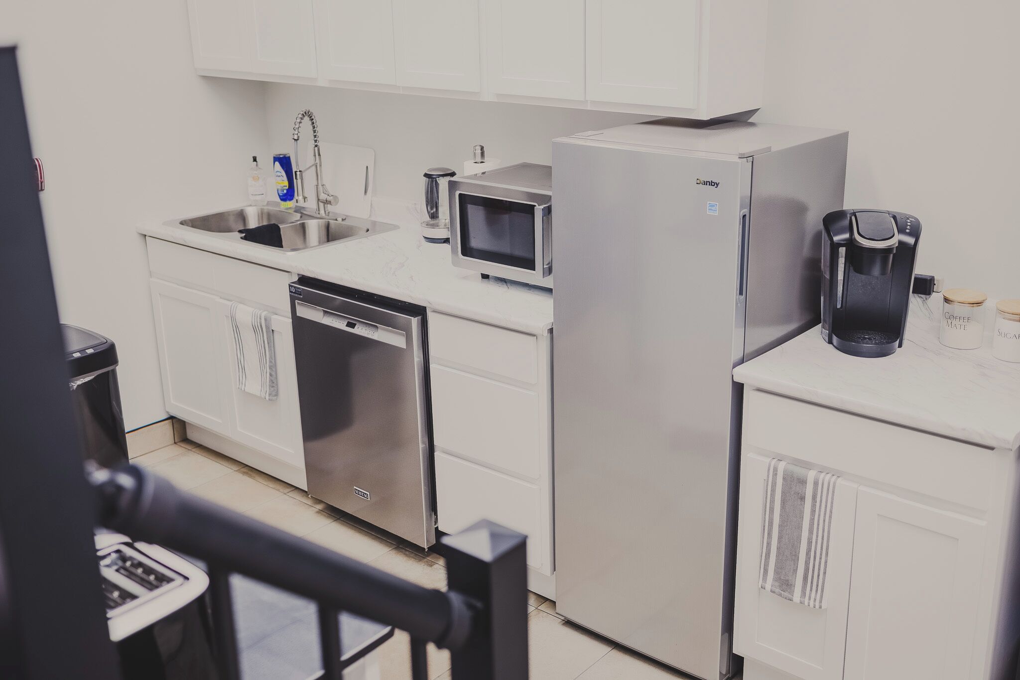 Een moderne keuken met een vaatwasser, magnetron, koelkast en koffiezetapparaat.