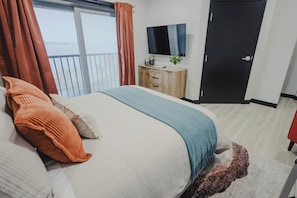A bedroom with a bed, a wooden dresser, a television, and a door.