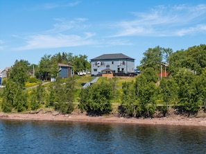 A large two-story house with a flat roof, located near a body of water.