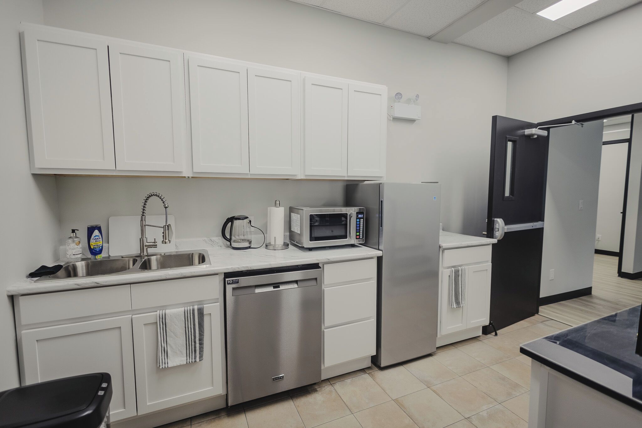 Una cocina moderna con gabinetes blancos, lavavajillas, microondas y refrigerador.