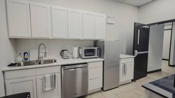 Una cocina moderna con gabinetes blancos, lavavajillas, microondas y refrigerador.