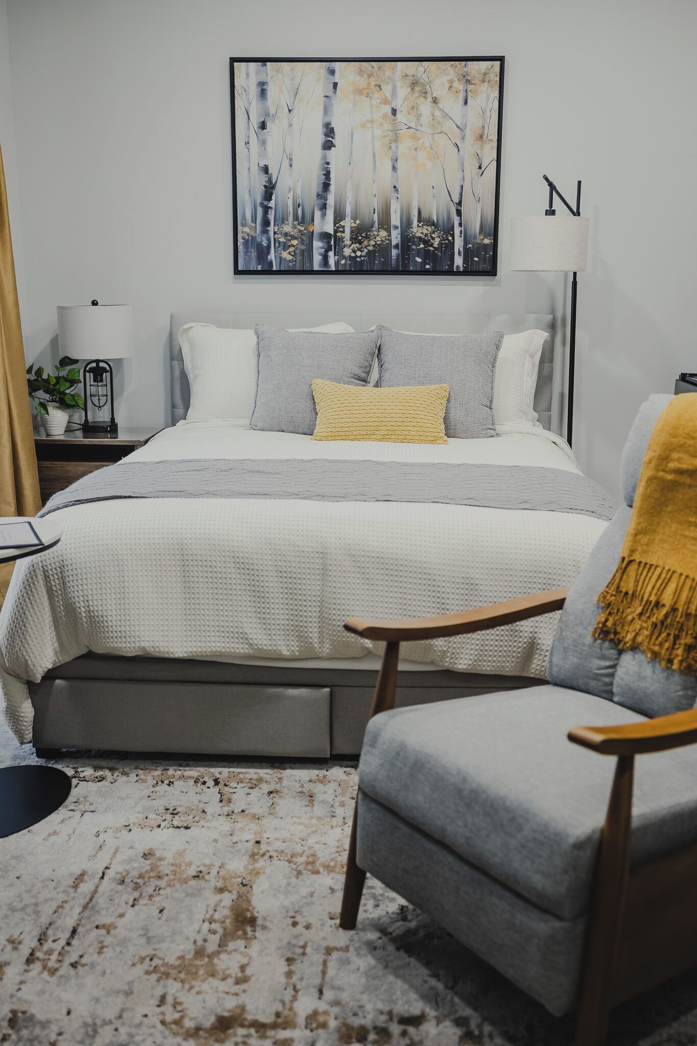 A bedroom with a bed, bedside tables, a lamp, a chair, a rug, and a painting on the wall.