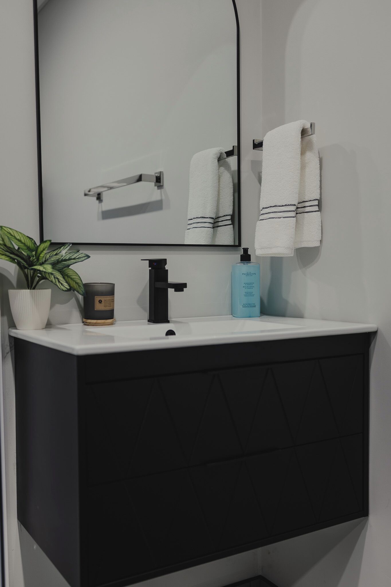 A bathroom with a white sink, black cabinet, a mirror, a potted plant, a candle, and a blue bottle.
