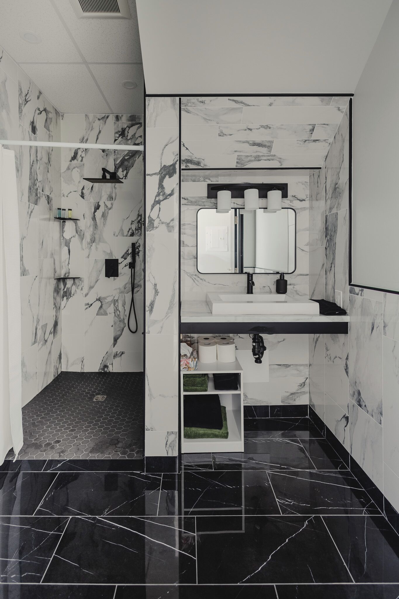 A modern bathroom with a shower, a sink with a mirror, and marble walls.