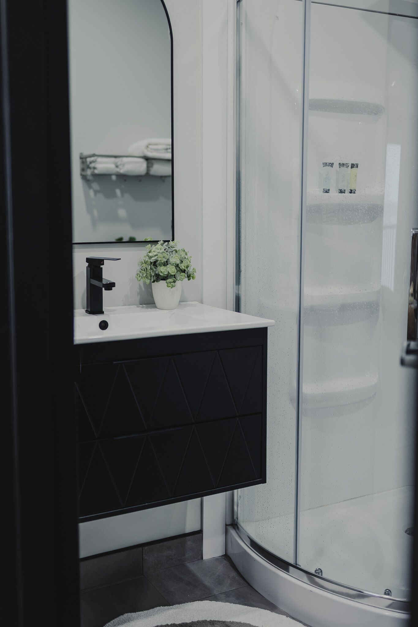 A bathroom with a white sink, black cabinet, and a glass shower enclosure.