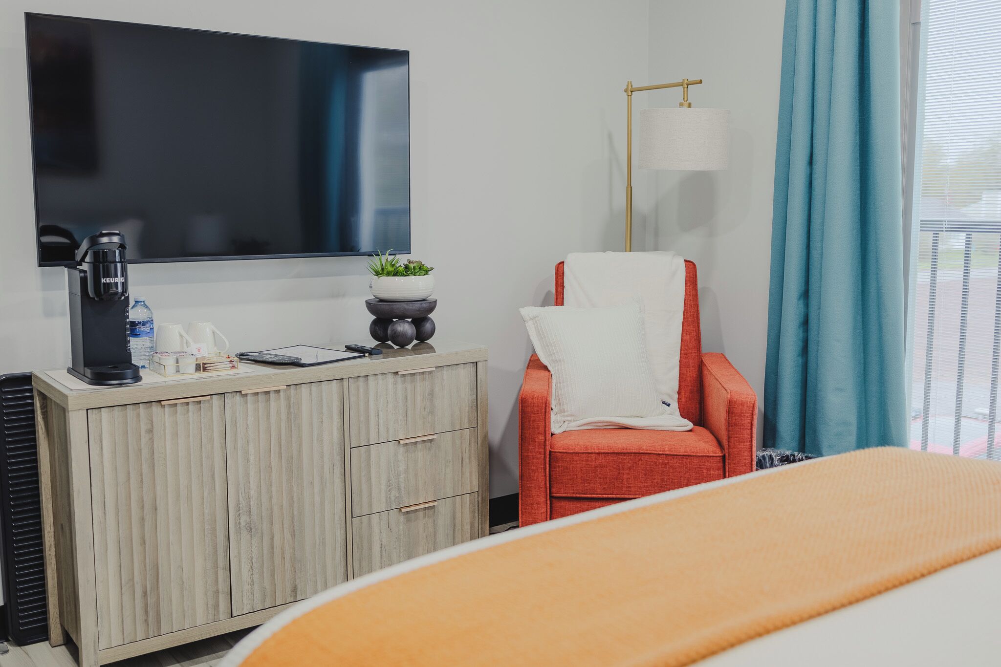 Een hotelkamer met een bed, een televisie, een bureau met koffiezetapparaat, een rode stoel en een raam met gordijnen.