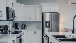 A modern kitchen with white cabinets, stainless steel appliances, and a marble countertop. - Falkenberg Business Centre and Suites (Botwood)
