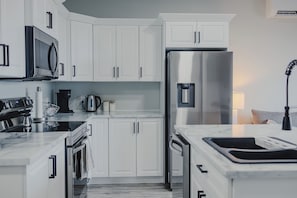 A modern kitchen with white cabinets, stainless steel appliances, and a marble countertop.