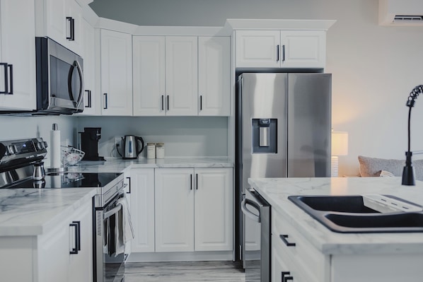 A modern kitchen with white cabinets, stainless steel appliances, and a marble countertop.