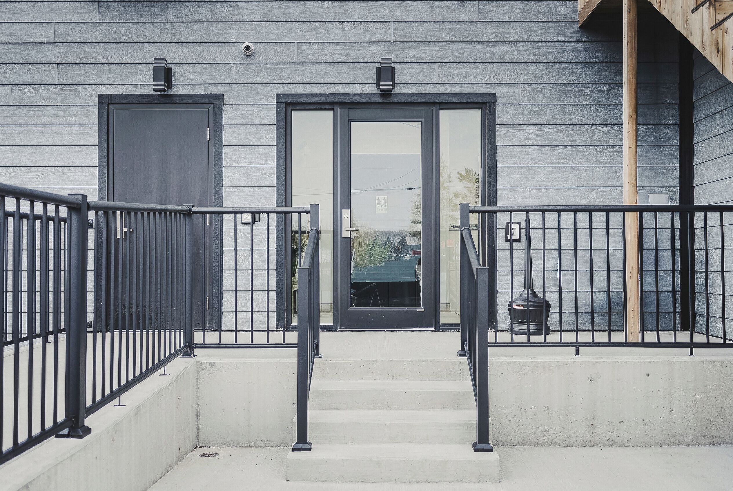 A building entrance with a concrete staircase, metal railings, and two doors.