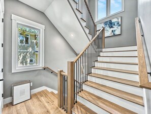 Eine Treppe mit Holzstufen und Metallgeländern, ein Fenster mit Blick auf ein Haus und ein Gemälde an der Wand.
