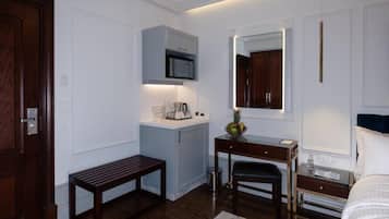 Habitación de hotel con puerta de madera, un escritorio con espejo, una banca, una cama y una pequeña zona de kitchenette.
