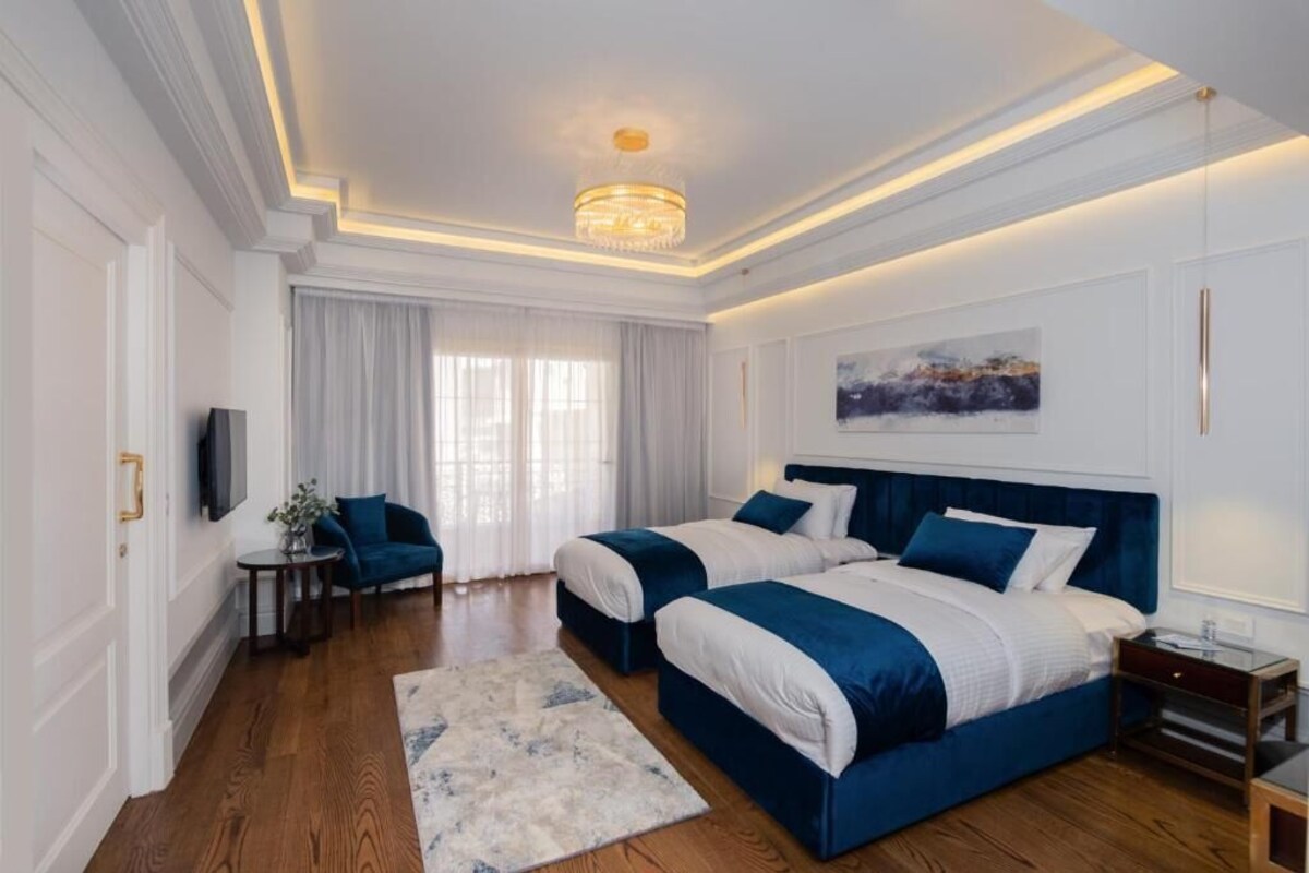 A modern bedroom with two beds, a chandelier, and a painting on the wall.