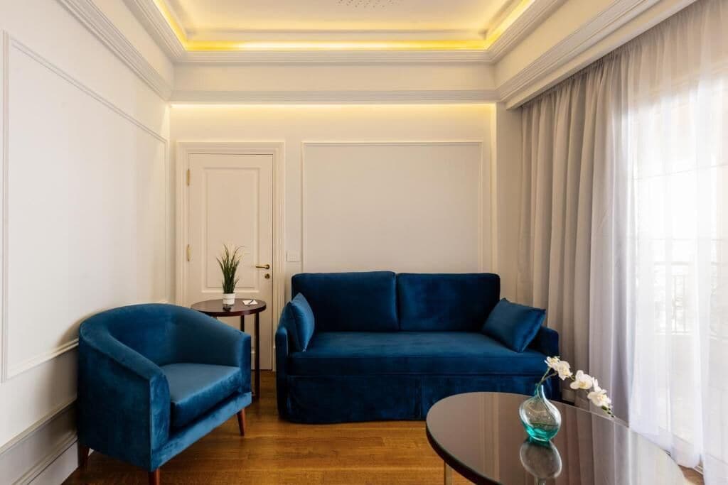 A room with a blue sofa, a blue armchair, and a small table with a vase.