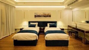 A hotel room with two beds, a desk, a chair, a chandelier, and a painting on the wall. - Maran Residence (Cairo Governorate)