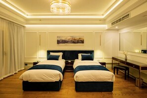 Quarto de hotel com duas camas, uma escrivaninha, uma cadeira, um candelabro e um quadro na parede.