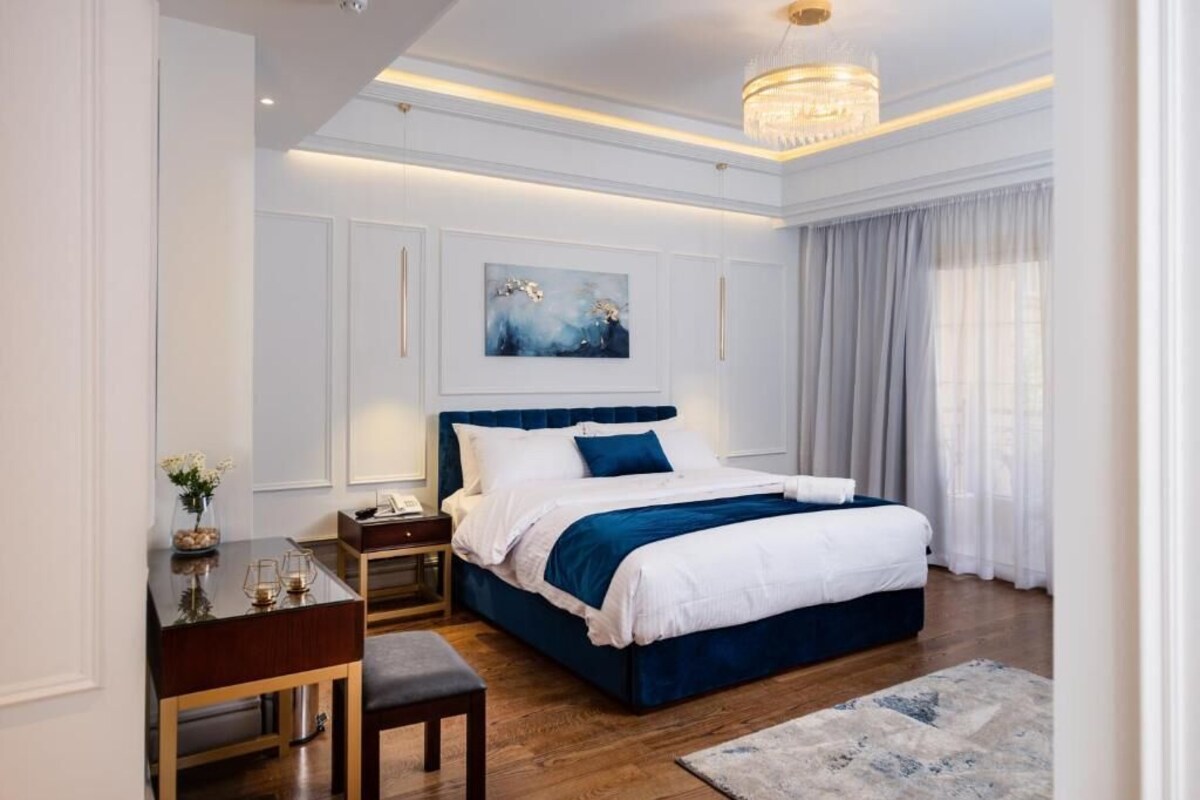 A modern bedroom with a large bed, bedside tables, a desk, and a chandelier.