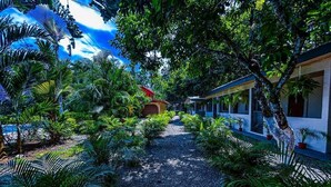 A pathway lined with tropical plants leading to a building with a red roof and a white exterior. - Iguana Villas (Puerto Viejo de Talamanca)