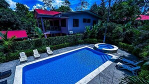 A swimming pool with lounge chairs, a hot tub, and a house with a red roof. - Iguana Villas (Puerto Viejo de Talamanca)