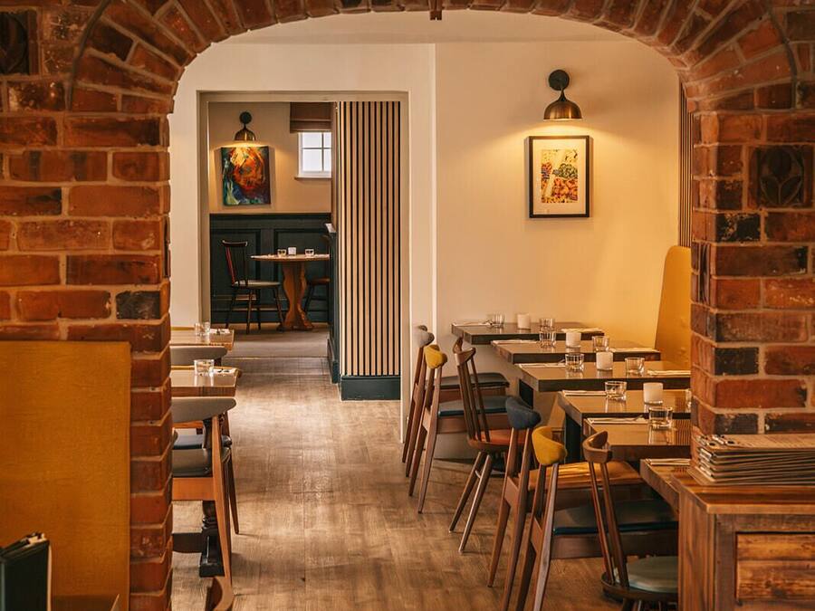A restaurant with brick arches, wooden tables, and chairs.