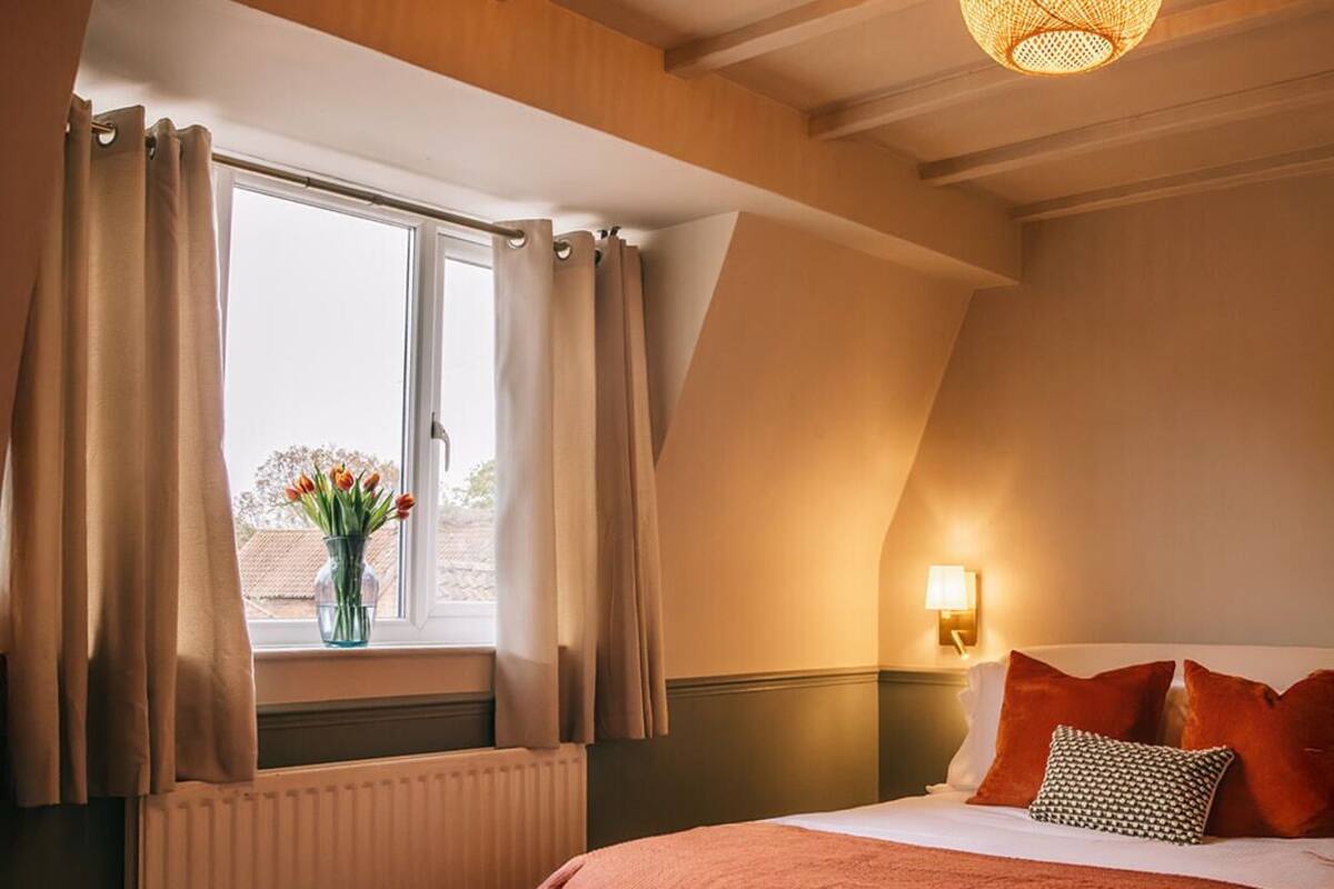A bedroom with a bed, a window with curtains, a wall-mounted lamp, and a ceiling light fixture.