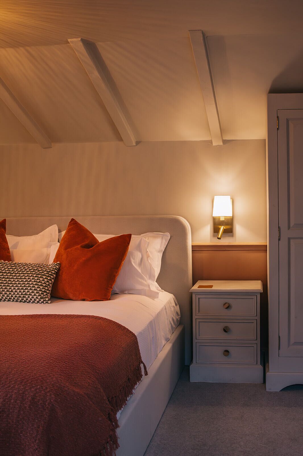 Ein Schlafzimmer mit Bett, Kissen, Nachttisch und einer Wandlampe.