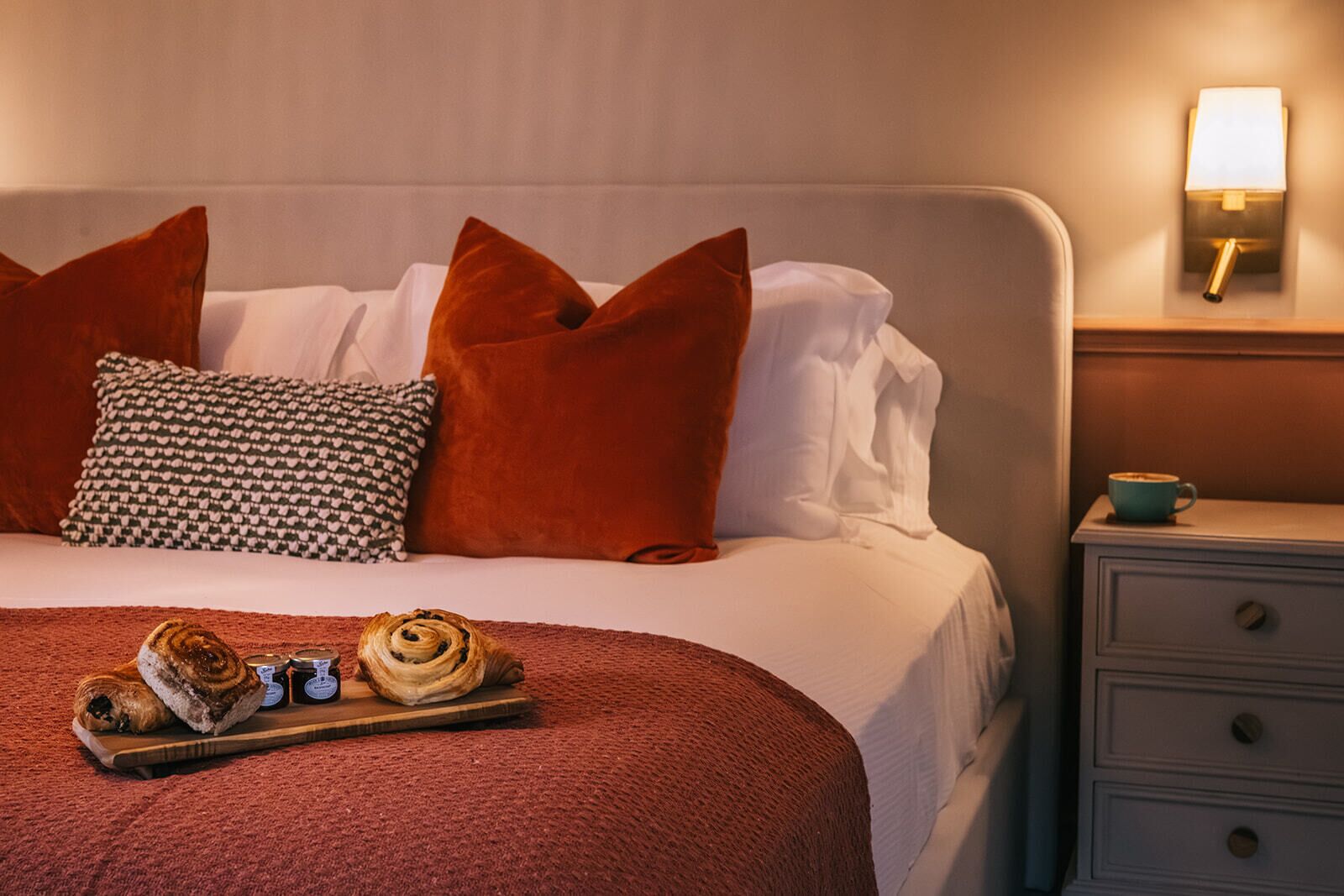 Una cama bien hecha con un edredón rojo, almohadas blancas y una bandeja con pasteles.