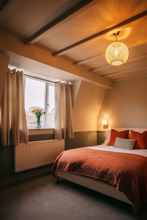 A bedroom with a bed, a window with curtains, a wall-mounted lamp, and a ceiling light fixture.