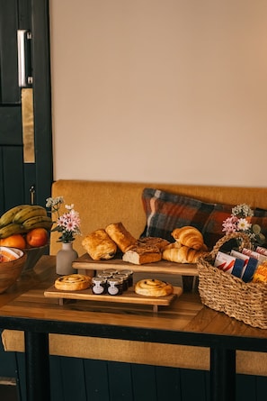 A wooden table with pastries, a bowl of fruit, and a vase of flowers.