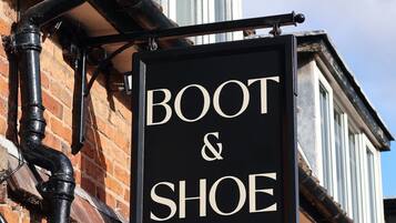 A black sign with 'BOOT & SHOE' written on it, attached to a brick building with a window and a metal gutter.