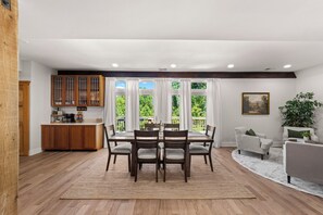 Un comedor con mesa y sillas de madera, una cocina con armarios de madera, y vistas a la vegetación a través de amplios ventanales.