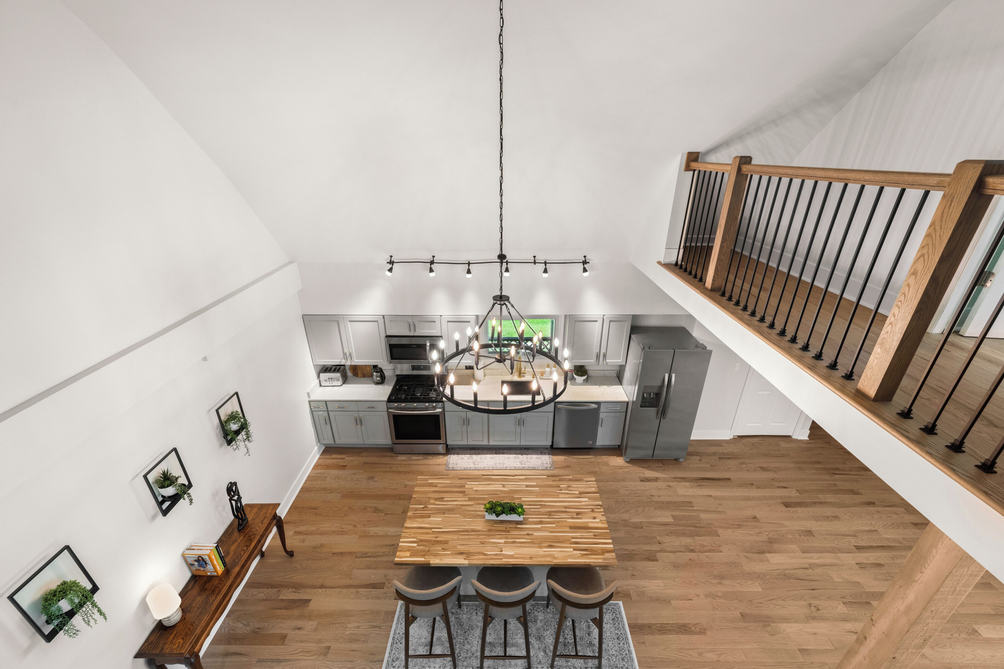 A modern kitchen with a central island, wooden flooring, and a staircase with a wooden railing.