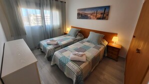 A hotel room with two beds, a desk, a painting, and a view of the beach. - Crisol (Los Cristianos)
