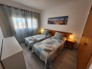Ein Hotelzimmer mit zwei Betten, einem Schreibtisch, einem Gemälde und Blick auf den Strand.