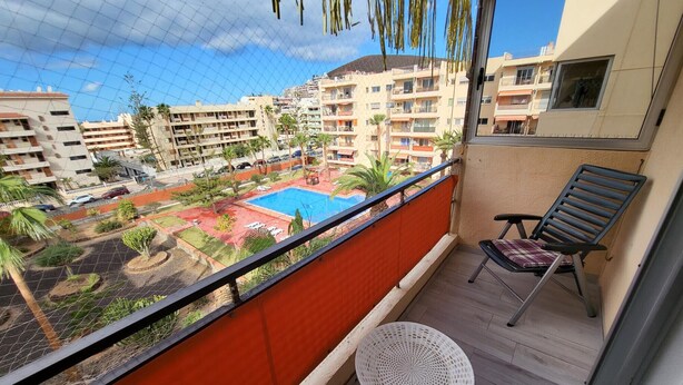 A balcony with a view of a swimming pool, a chair, and a small table. - Crisol (Los Cristianos)